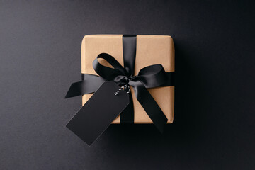Gift box with black bow and price tag on black background.