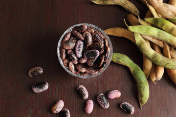 Top down view of scarlet runner bean in a small crystal glass bowl on a dark surface. In the...