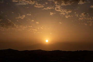 Bright big sun on the sky with yellow orange gradient colors with clouds and bright sky at the sunset in algeria desert