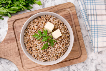 Boiled buckwheat in a plate with parsley leaf and butter on a white.
