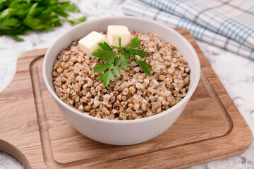 Boiled buckwheat in a plate with parsley leaf and butter on a white.