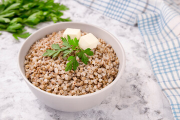 Boiled buckwheat in a plate with parsley leaf and butter on a white.