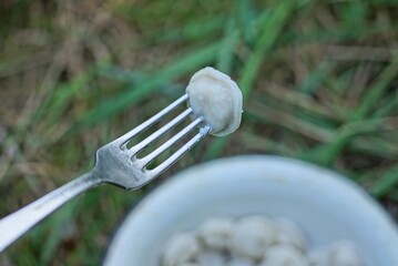 one gray metal fork with white round dumplings over a plate in green grass