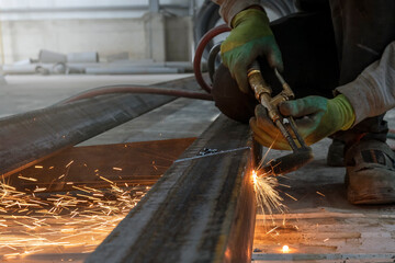 The worker is manual cutting to a carbon steel profile with oxy-acetylene process. Welding, or gas welding in the U.S. and oxy-fuel cutting are processes that use fuel gases and oxygen to weld.