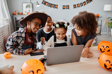 Portrait of happy African-American kids wearing Halloween costumes while using laptop at home and...