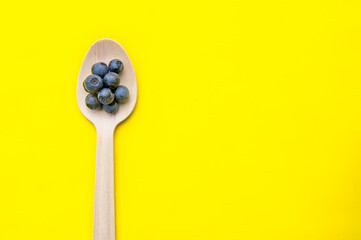 Flat lay of recycled spoon and juicy, fresh blueberries on color table. Space for text. Isolated ripe sweet bilberry fruits in eco spoon on yellow background. Copy Space. Healthy raw vegetarian food 