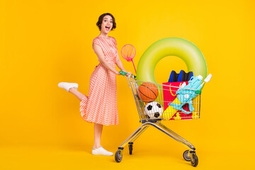 Photo of excited client girl step carry supermarket cart wear striped dress sneakers isolated...
