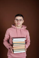 Funny student nerd in glasses with books in hands. Brown background. Preparing for exams in the library.