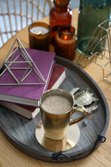 Wooden tray with decorations, books and hot drink on table