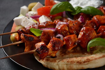 Fried souvlaki, greek salad and tzatziki on wooden table. Chicken skewers souvlaki, pita bread - delicious greek style lunch on a dark background