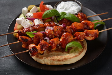 Fried souvlaki, greek salad and tzatziki on wooden table. Chicken skewers souvlaki, pita bread - delicious greek style lunch on a dark background