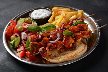 Fried souvlaki, greek salad and tzatziki on wooden table. Chicken skewers souvlaki, pita bread - delicious greek style lunch on a dark background