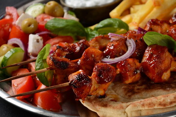 Fried souvlaki, greek salad and tzatziki on wooden table. Chicken skewers souvlaki, pita bread - delicious greek style lunch on a dark background