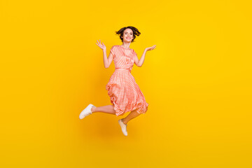 Photo of excited energetic girl jump raise arms wear striped dress sneakers isolated yellow color...