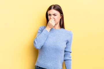 hispanic pretty woman feeling disgusted, holding nose to avoid smelling a foul and unpleasant stench