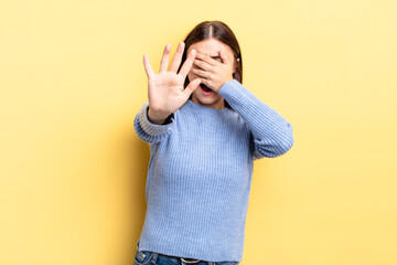 hispanic pretty woman covering face with hand and putting other hand up front to stop camera,...