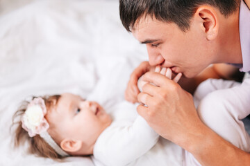 Fototapeta na wymiar a newborn girl is lying with her young father in a snow-white bed. dad kisses the hands of his newborn daughter. the concept of the family