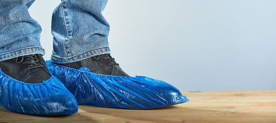 Man with blue shoe covers worn over classic shoes on gray background, closeup. Photo with copy...
