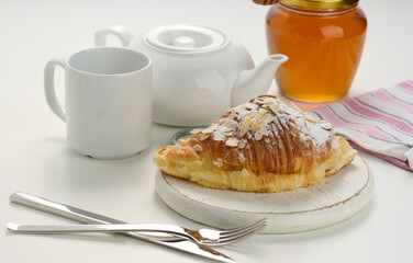 Baked crisp croissant is sprinkled with sugar powder and almond flakes on a wooden board, white ceramic brew and a cup on a white table. Breakfast