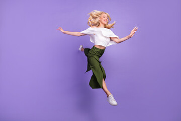 Full length body size photo blonde girl jumping up smiling doing stretching gracefully isolated pastel violet color background