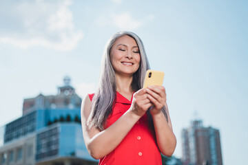 Photo of mature attractive asian woman happy positive smile look read browse smartphone urban...