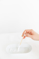 a wooden stick is placed in an oval saucer with a cosmetic cream. there are several cream textures in a white saucer on a white background. Cosmetology and care.