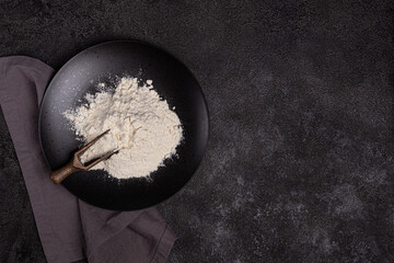 Wheat flour in a black plate on a dark background. The ingredient. Bakery products.