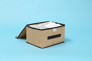 Textile storage case with folded clothes on light blue background