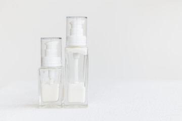 two glass cream bottles with a dispenser lid stand on a white cube. White cream inside transparent containers. Home and professional skin care.