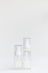 two glass cream bottles with a dispenser lid stand on a white cube. White cream inside transparent containers. Home and professional skin care.