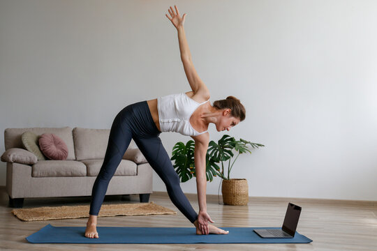 Sporty young woman practicing yoga in the comfort of her own home. Yogini performing morning physical exercise routine at the living room. Interior background, copy space, close up.