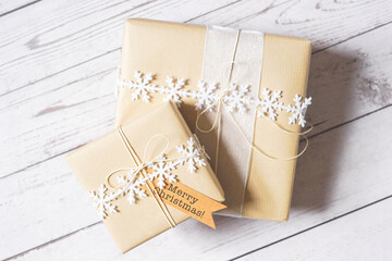 Christmas presents on white wooden background. Natural winter theme decoration, brown paper, twine, snowflake ribbon, tag. Sustainable gift wrapping. Gift giving. Merry Christmas.