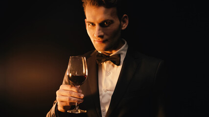 elegant young man in suit with bow tie holding glass of wine on black