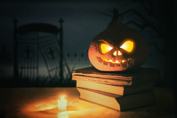 Festive scary halloween pumpkin on a stack of old books with candle