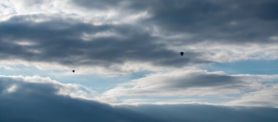 Dramatischer Himmel bei Sonnenuntergang mit Wolken. Ein Heißluftballon am Horizont zwischen der Wolkenschicht gegen einen blauen Streifen klaren Himmels.