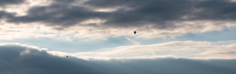 Dramatic sky during sunset with clouds. One hot-air balloon on the horizon between the cloud layer against a blue stripe of clear sky.