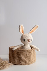 Crocheted bunny sits in a jute basket on a white background.