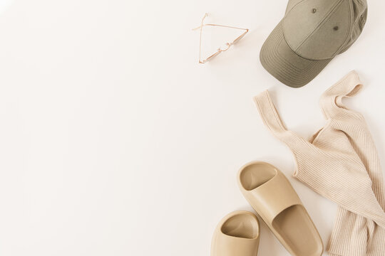Minimal fashion concept with sport women's clothes on white background. Neutral beige colour slippers, top, sunglasses, cap. Flat lay, top view