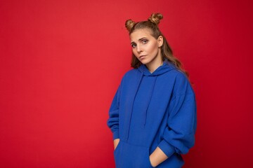 Portrait of dissatisfied offended young attractive winsome blonde woman with two horns with sincere emotions wearing casual bright blue hoodie isolated on red background with free space