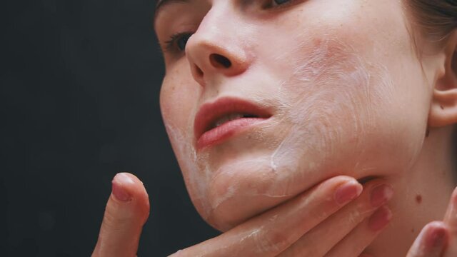 Closeup facial portrait of beautiful young adult woman massaging face applying organic foamy soap cleanser creme. Healthy skin concept.
