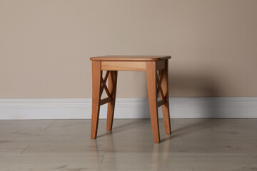 Stylish wooden stool near beige wall indoors