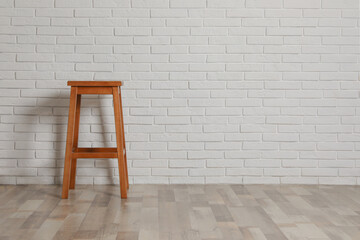 Stylish wooden stool near white brick wall indoors. Space for text
