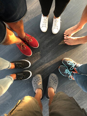 Group of young people feet stand in a circle. Five people in shoes and one barefoot