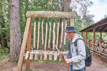 Mature man with backpack playing wooden xylophone on ecological trail