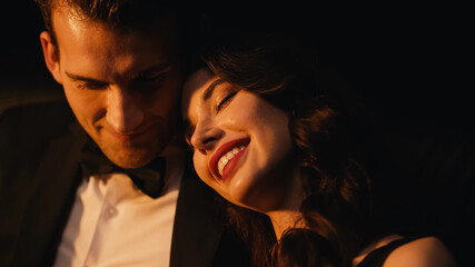 pleased young woman smiling while leaning on shoulder of boyfriend isolated on black