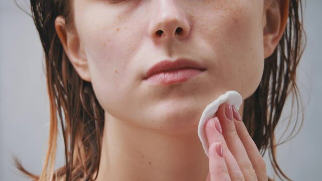 Young beautiful nude woman removing makeup using cotton pad, massaging skin gently cleansing, applying moisturizing lotion creme in bathroom.