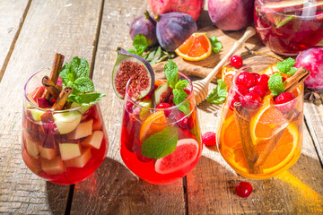 Traditional autumn winter drink hot spicy sangria - red, pink, white. With cider, pink red wine, apples, oranges, pomegranate, cranberry, plum, figs, cinnamon sticks. Wooden rustic table copy space