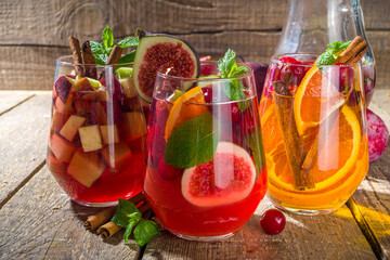 Traditional autumn winter drink hot spicy sangria - red, pink, white. With cider, pink red wine, apples, oranges, pomegranate, cranberry, plum, figs, cinnamon sticks. Wooden rustic table copy space