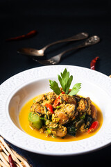 Thai Food concept Fried Mussels in yellow curry in white dish on black slate stone with copy space