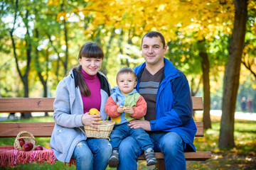 Fototapeta premium happy family enjoying autumn picnic. Father mother and son sit on bench with apples basket. Happy family leisure together concept